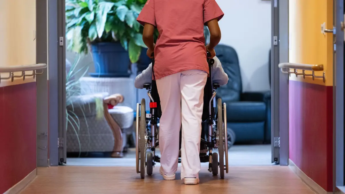 Pflegerin und Patientin: ARCHIV - 07.02.2024, Baden-Württemberg, Filderstadt: Eine Bewohnerin eines Pflegeheims wird von einer Pflegerin einen Gang entlang geschoben. (zu dpa: «Institut: Ohne Zuwanderung droht Wohlstandsverlust im Osten») Foto: Marijan Murat/dpa +++ dpa-Bildfunk +++