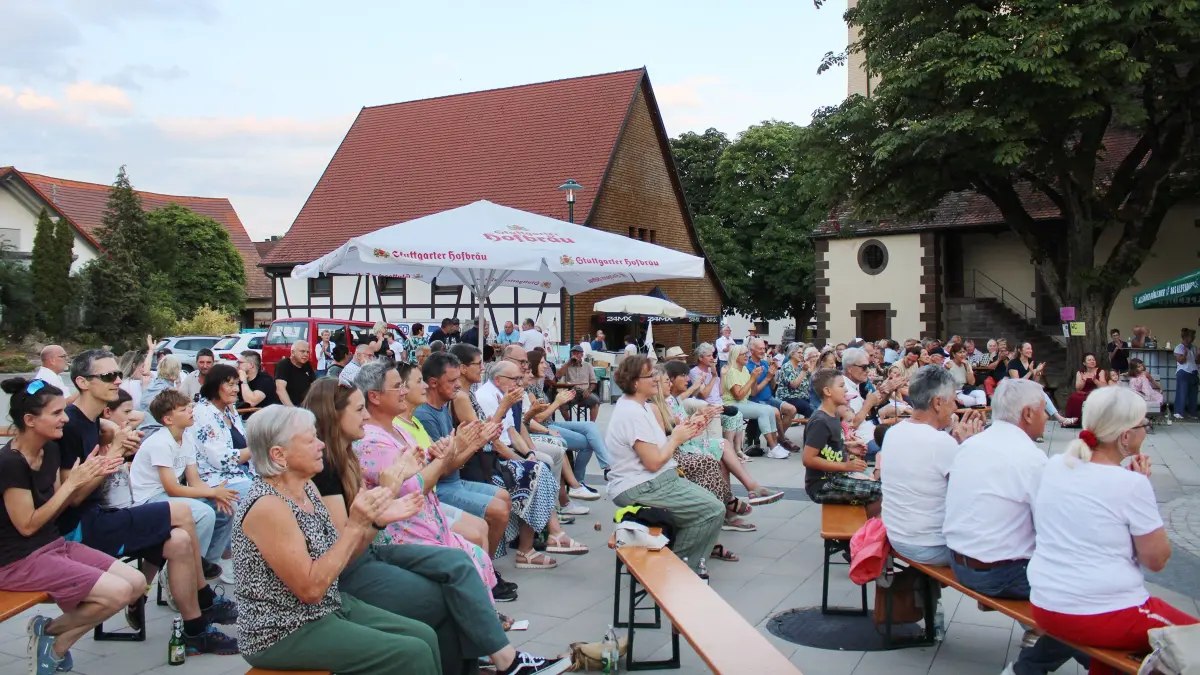 4103: Zahlreiche Besucher fanden auf dem Dorfplatz je nach Belieben einen Sitz- oder Stehplatz im Schatten oder in der Sonne, um den Abend zu genießen.