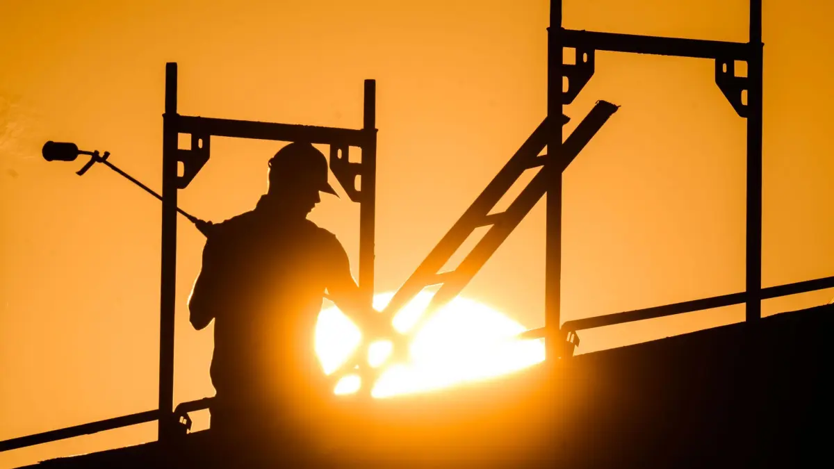 Ein Bauarbeiter im Gegenlicht der Sonne auf einem Gerüst: ARCHIV - 12.08.2022, Niedersachsen, Hannover: Die Baubranche ist offen für ungelernte Kräfte. (zu dpa: «Versicherung: Hitze sorgt für mehr Unfälle») Foto: Julian Stratenschulte/dpa/dpa-tmn +++ dpa-Bildfunk +++