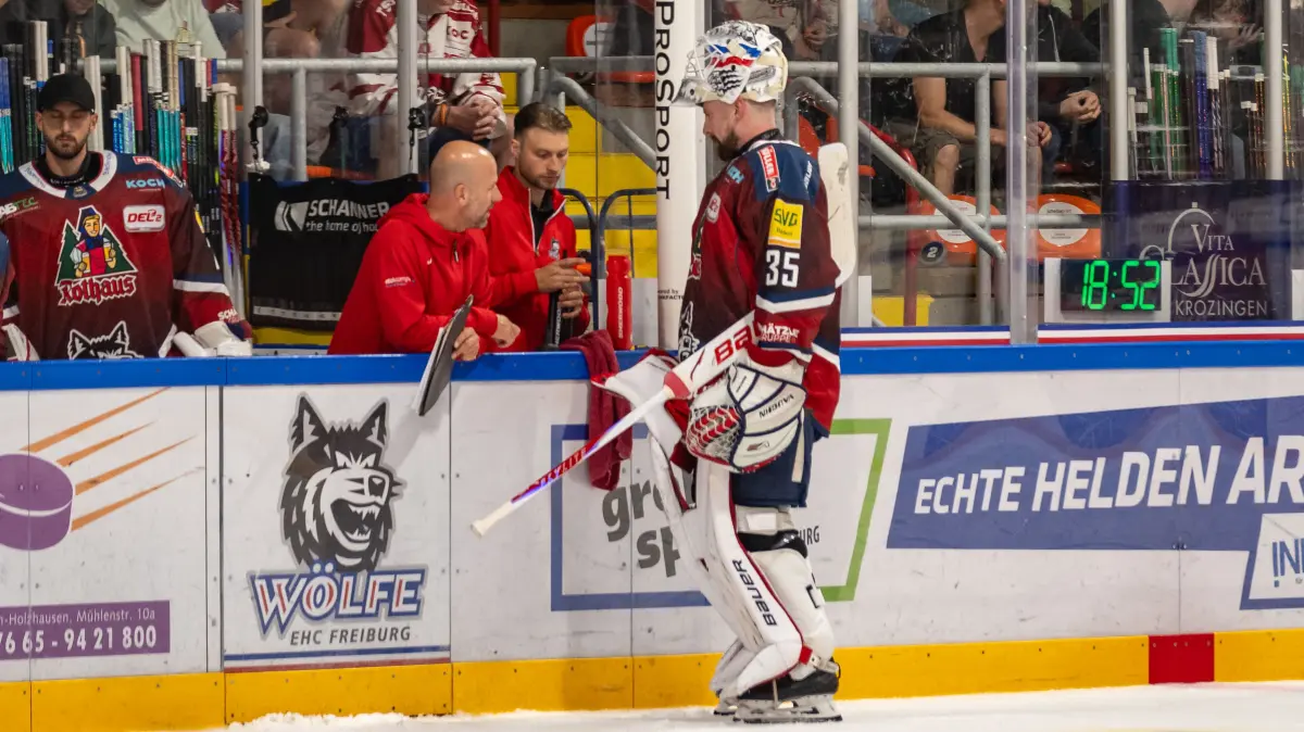 Olafr Schmidt (EHC Freiburg, #35) im Gespräch mit Trainern an der Bande.