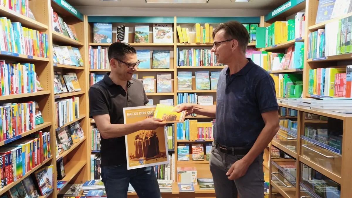 VHS-Leiter Thomas Gähme überreicht Daniel Bäurer von Mory's Hofbuchhandlung das neue Programmheft.