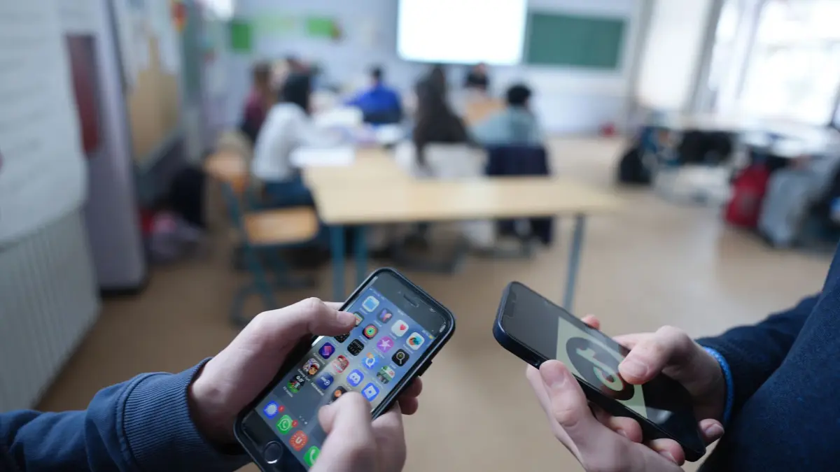 Smartphones in der Schule: ILLUSTRATION - 13.02.2026, Hamburg: Zwei Schüler stehen in einem Klassenraum und schauen auf ihre Smartphones, auf einem der Displays ist das Logo der Social-Media-Plattform TikTok zu sehen. (zu dpa: «Hessens Schulen führen Medienführerschein ein») Foto: Marcus Brandt/dpa +++ dpa-Bildfunk +++
