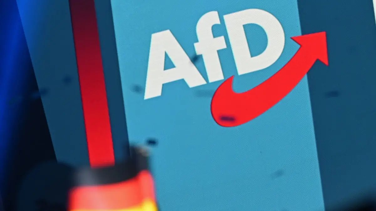 Wahlkampf Sachsen-Anhalt - AfD: 05.09.2026, Sachsen-Anhalt, Magdeburg: Ein Logo der AfD steht auf einer Wand auf einer Bühne beim AfD-Wahlkampfabschlusses im AMO Kultur- und Kongresshaus. Im Vordergrund ist eine Deutschlandfahne zu sehen. Foto: Michael Brandt/dpa +++ dpa-Bildfunk +++