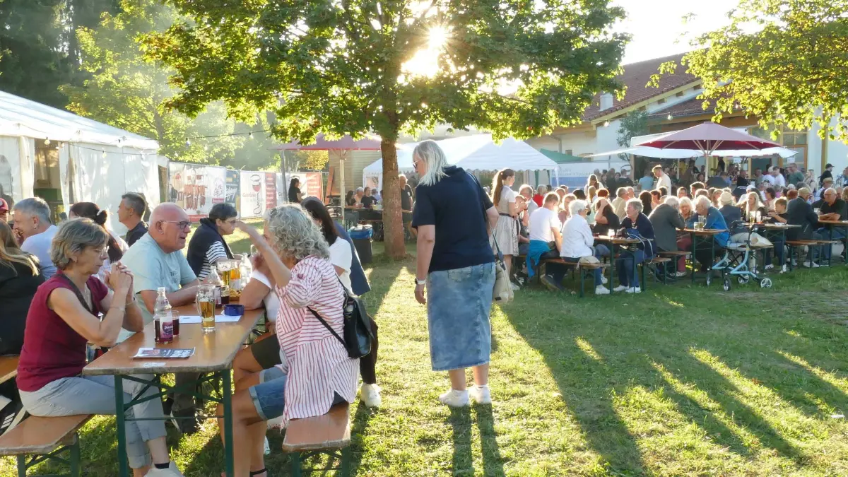 Viele Besucher genießen den lauen Sommerabend vor dem Festzelt in der Abendsonne bei der Backhaushockete des Musikvereins Marschalkenzimmern.