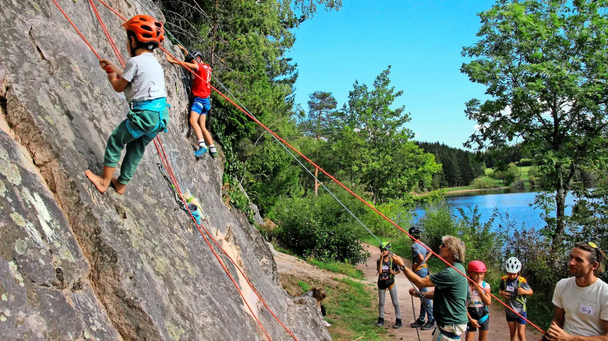 Den Kirnbergsee im Rücken: Kinder klettern mit Helmen und mit Seilen gesichert die Felswand nach oben.