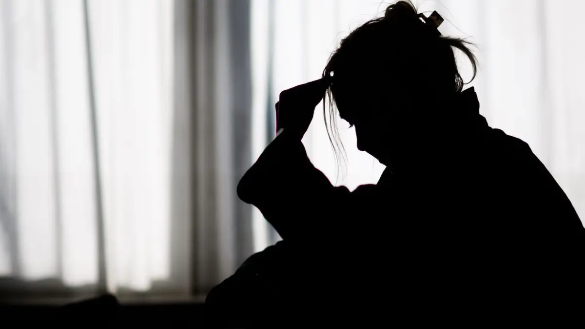 Die Silhouette einer Frau zeichnet sich vor einer hellen Fensterfront ab (gestellte Szene).