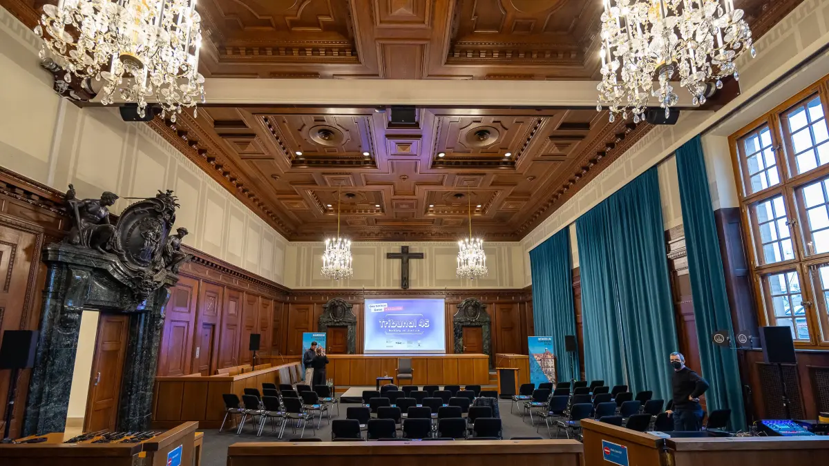 Innenansicht des historischen Saals 600 im Justizpalast Nürnberg, bekannt als zentraler Schwurgerichtssaal der Nürnberger Prozesse nach dem Zweiten Weltkrieg. Der Raum ist mit Holzvertäfelung, Kronleuchtern und grünen Vorhängen ausgestattet.