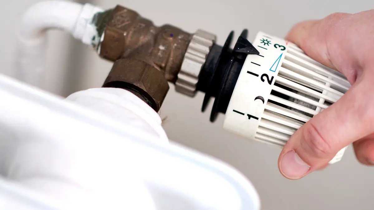 Thermostat-Ventil an einem Heizkörper: ARCHIV - 07.03.2019, Niedersachsen, Hannover: Eine Frau dreht am Thermostat einer Heizung. (zu dpa: «Prognose: Heizkosten steigen 2026 an») Foto: Hauke-Christian Dittrich/dpa +++ dpa-Bildfunk +++