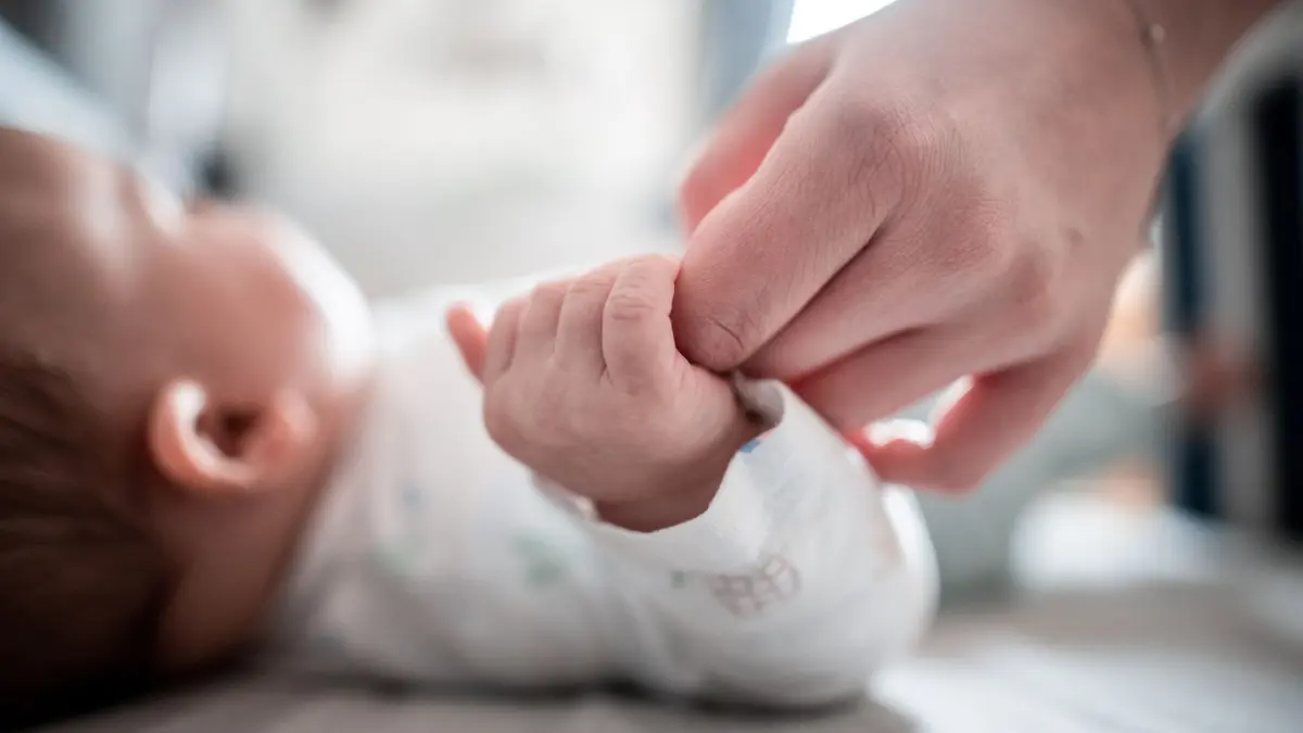 Ein Baby klammert sich an den Finger seiner Mutter: Wie soll das Baby heißen? Ob ein Name beliebt oder eher ungewöhnlich ist, erfahren Eltern beim Studium von Namenshitlisten. (zu dpa: «Klingt schön, passt er aber auch? Die Tücken der Namenswahl»)