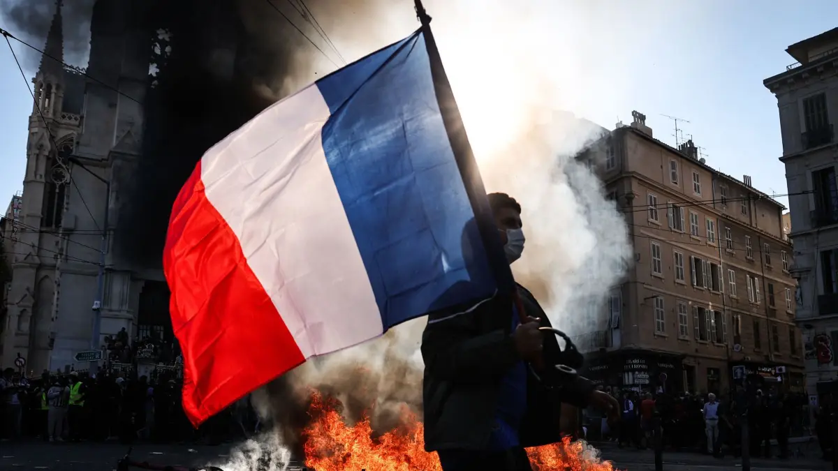 Protesttag in Frankreich: Ein Demonstrant, der eine französische Nationalflagge schwenkt, geht während Zusammenstößen vor Beginn einer Demonstration gegen die „hohen Lebenshaltungskosten“ an einem Feuer vorbei. Die Aktion ist Teil eines landesweiten Mobilisierungsaufrufs, der verschiedene Gruppen zusammenbringt. (zu dpa: «Frankreichweite Proteste: Erste Zusammenstöße mit Polizei»)