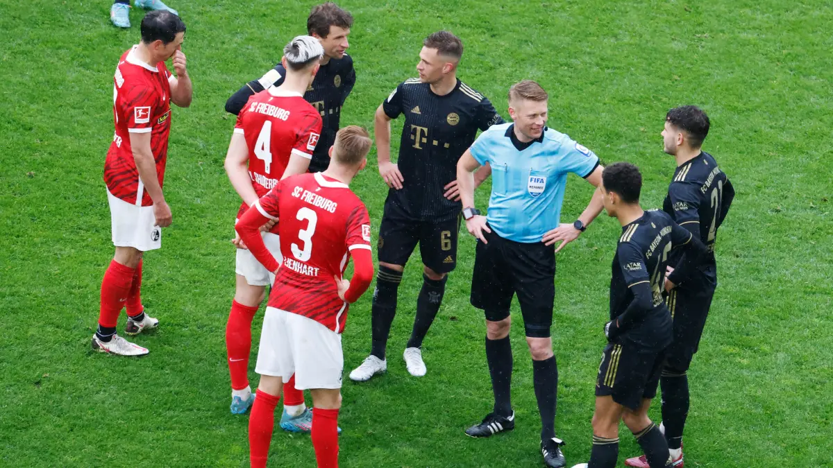 02.04.2022, Baden-Württemberg, Freiburg im Breisgau: Fußball: Bundesliga, SC Freiburg - Bayern München, 28. Spieltag, Europa-Park Stadion: Schiedsrichter Christian Dingert (in blau) steht gemeinsam mit Spielern dass SC Freiburg und des FC Bayern München während einer Spielpause auf dem Feld. Foto: Philipp von Ditfurth/dpa - WICHTIGER HINWEIS: Gemäß den Vorgaben der DFL Deutsche Fußball Liga bzw. des DFB Deutscher Fußball-Bund ist es untersagt, in dem Stadion und/oder vom Spiel angefertigte Fotoaufnahmen in Form von Sequenzbildern und/oder videoähnlichen Fotostrecken zu verwerten bzw. verwerten zu lassen. +++ dpa-Bildfunk +++