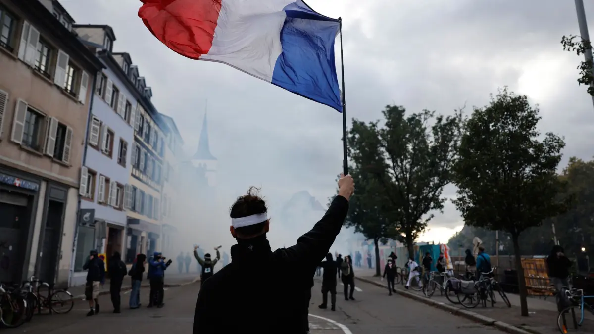 Proteste in Straßburg: 24.10.2026, Frankreich, Straßburg: Ein Demonstrant hält während einer Demonstration gegen steigende Lebenshaltungskosten eine französische Flagge hoch. Foto: Jean-Francois Badias/AP/dpa +++ dpa-Bildfunk +++