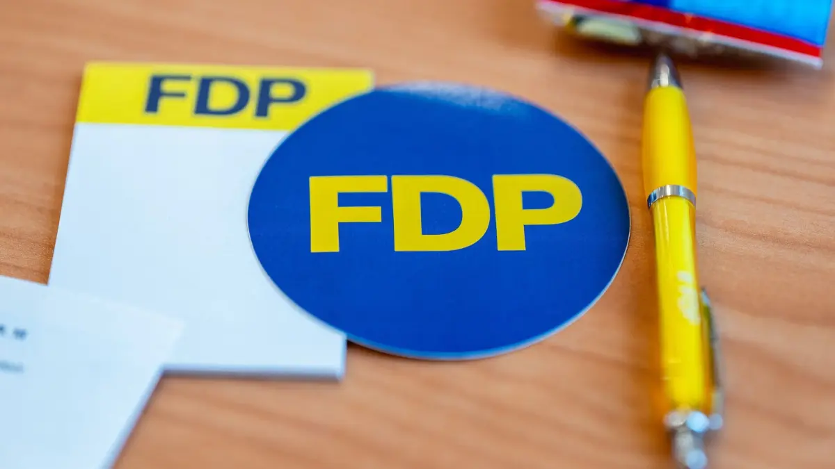 FDP Thüringen - Landesparteitag in Bleicherode: 24.10.2026, Thüringen, Bleicherode: Giveaways der FDP, darunter ein Aufkleber mit dem Parteilogo und ein Kugelschreiber, liegen auf den Tischen der Delegierten beim Landesparteitag der FDP Thüringen im Kulturhaus Bleicherode. Die Thüringer Liberalen kommen zu ihrem Landesparteitag zusammen. Foto: Jacob Schröter/dpa +++ dpa-Bildfunk +++