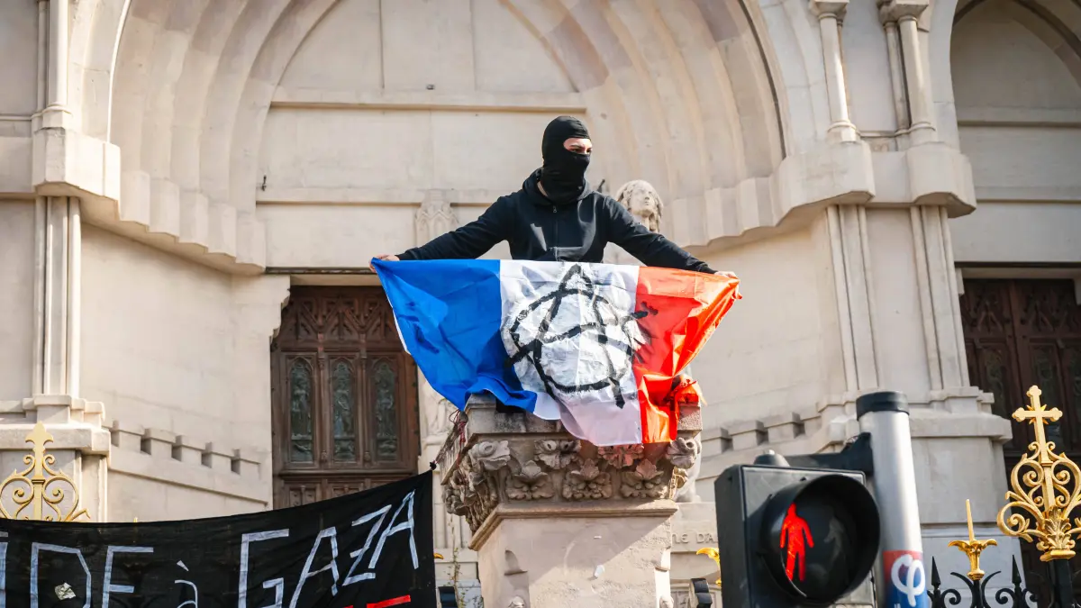 Marseille France Street Protests: Marseille France Street Protests A protester holds a French flag atop a monument during unrest in Marseille, France on October 24, 2026. Authorities deployed around 70,000 security personnel across France for renewed protests over the cost of living, after unrest a week earlier saw public buildings damaged, hundreds of shops looted and about 2,700 people arrested. Marseille Provence-Alpes-CÃ te France Copyright: xNaelxChahinex