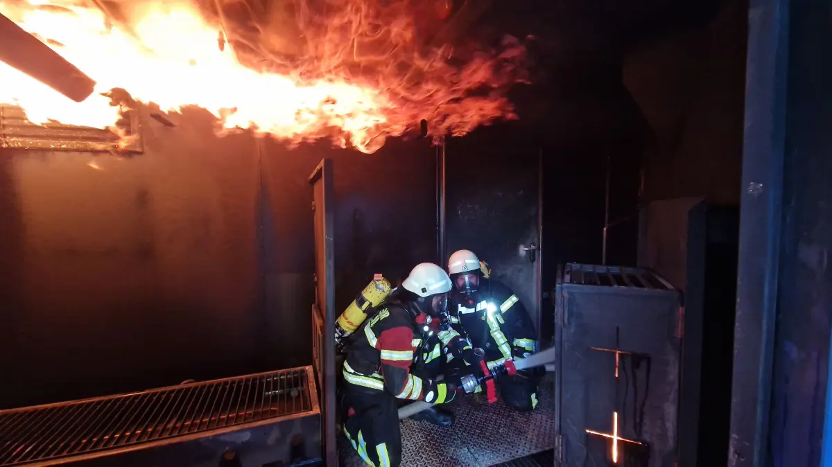 In der simulierten Hölle: Bei Temperaturen von bis zu 300 Grad kämpfen sich die Atemschutzgeräteträger Lukas Müller und Moritz Asprion durch den dichten Rauch des Brandcontainers. Direkt über ihren Köpfen schlagen die Flammen einer simulierten Rauchgasdurchzündung (Flashover) entlang.