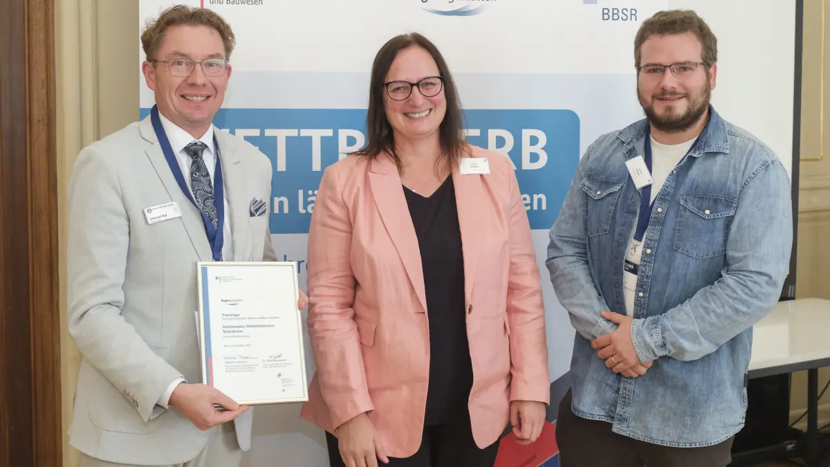 Bürgermeister Michael Ruf (links) und Projektleiter Sebastian Rittner (rechts) nehmen bei der Preisverleihung in Bonn die offizielle Urkunde für den „Multimodalen Mobilitätsknoten Baiersbronn“ aus den Händen von Melanie Schade (BBSR) entgegen.